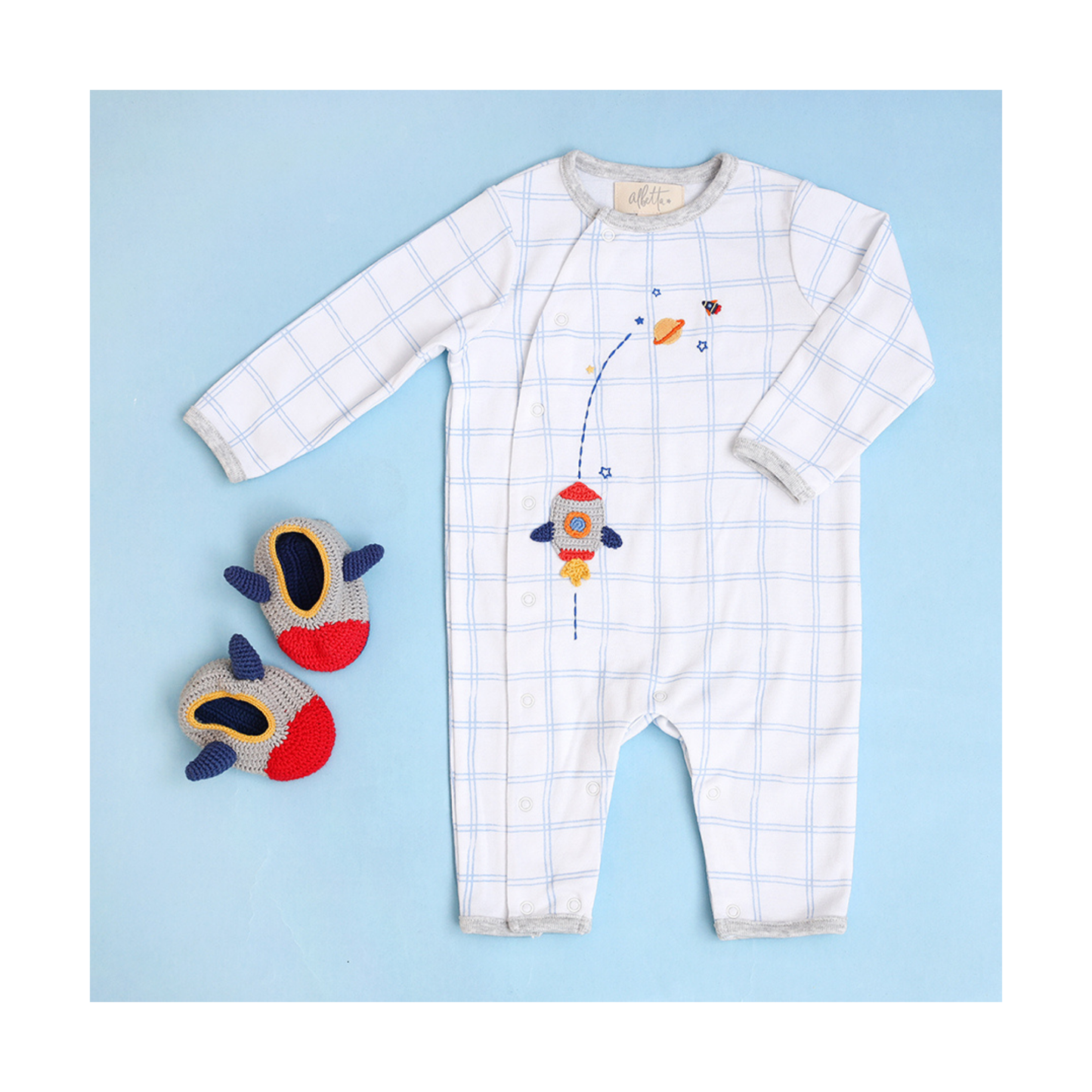 A babygro from Albetta Creations featuring applique crochet Rocket and space icons on a white and blue check background.