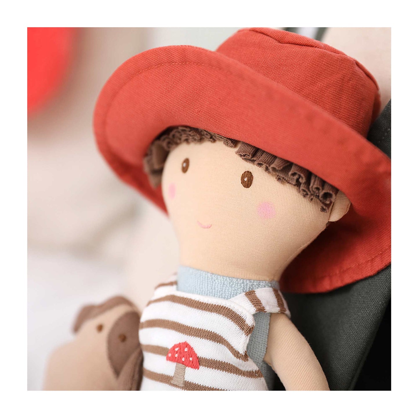 A super soft jersey doll with a linen hat and detached dog friend. Hugo wears a striped romper with a mushroom embroidered on the front and a red hat.